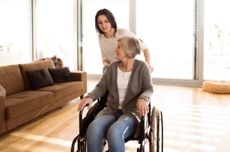 Young woman pushing elderly on a wheelchair.