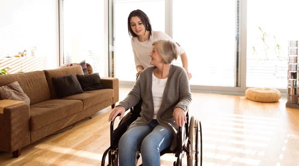 Young woman pushing elderly on a wheelchair.