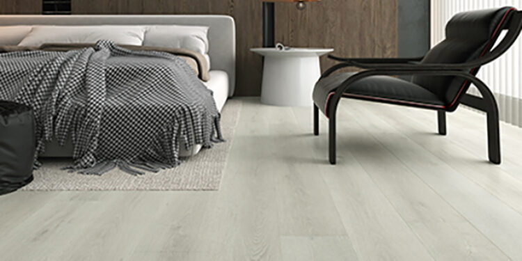 Minimalist bedroom interior featuring pale Eclipse Aqua Schild laminate flooring, upholstered low-profile bed, black lounge chair, white side table and dark wood feature wall.