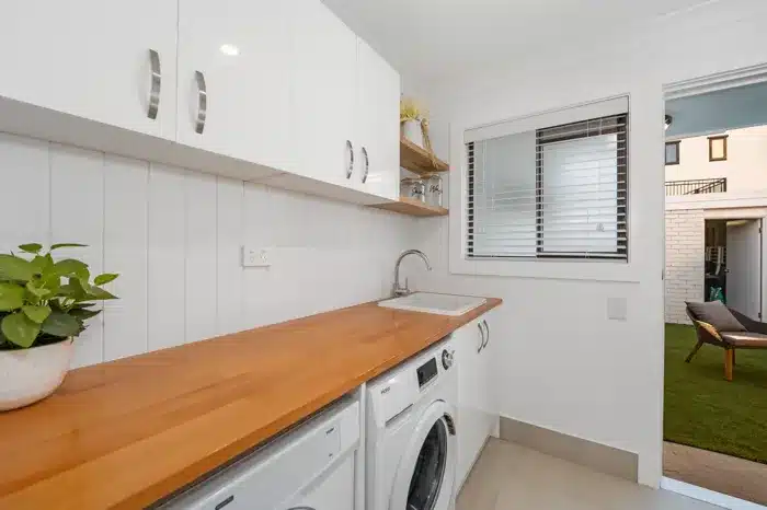 Modern laundry renovation with timber benchtop, overhead cabinets and washer-dryer combo